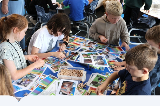 Open https://houseofscience.nz/ House of science - kids looking at cards on a school table